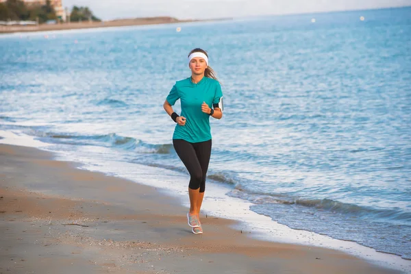 Joven chica deportiva corriendo en la playa al amanecer en la mañana — Foto de Stock