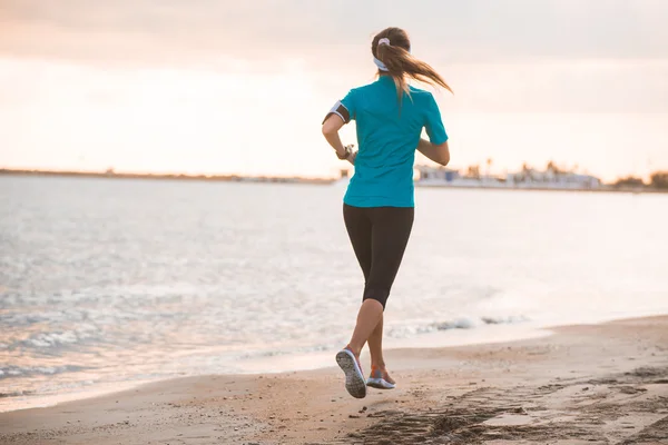 Joven chica en forma corriendo en la playa al amanecer en la mañana — Foto de Stock