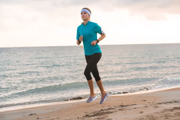 Joven chica en forma corriendo en la playa al amanecer en la mañana — Foto de Stock