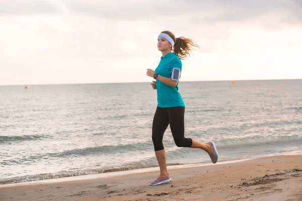 Joven chica en forma corriendo en la playa al amanecer en la mañana — Foto de Stock