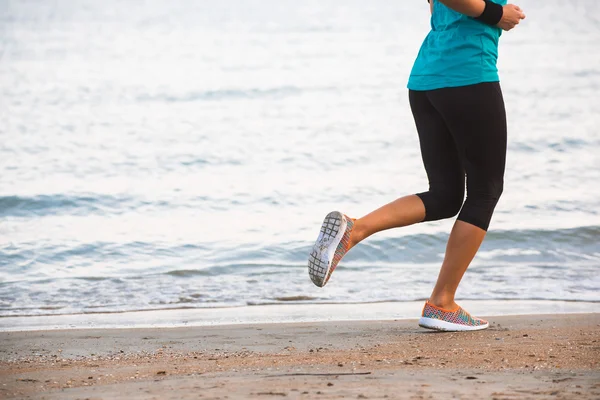 Primer plano de las piernas femeninas corriendo en la playa al amanecer en la mañana — Foto de Stock