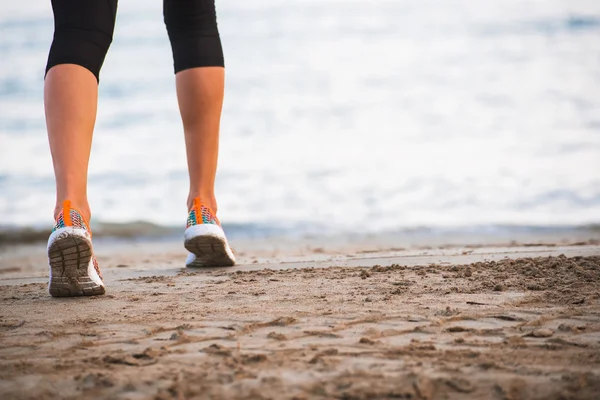 Primer plano de las piernas femeninas corriendo en la playa al amanecer en la mañana — Foto de Stock
