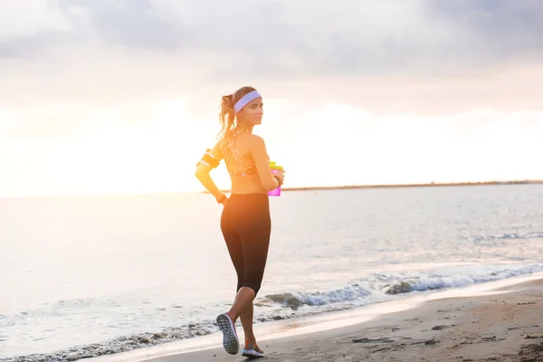 Joven chica en forma corriendo en la playa al amanecer — Foto de Stock