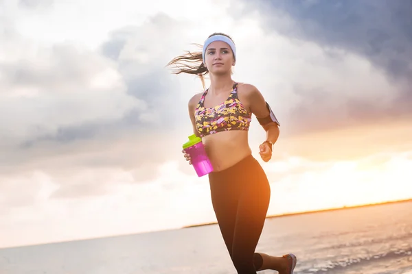 Joven chica en forma corriendo en la playa al amanecer — Foto de Stock