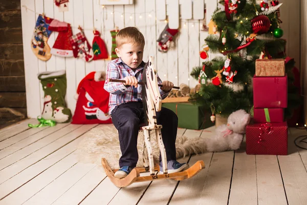 Kleiner Junge reitet Schaukelpferd aus Holz vor Weihnachtsbaum — Stockfoto