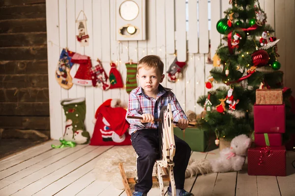 Kleiner Junge reitet Schaukelpferd aus Holz vor Weihnachtsbaum — Stockfoto