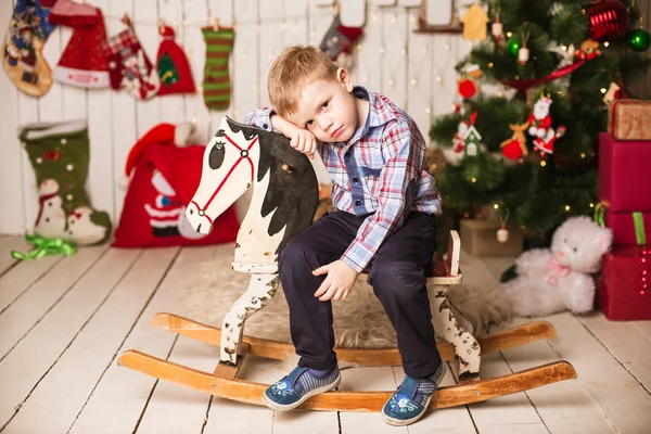 Kleiner Junge reitet Schaukelpferd aus Holz vor dem Weihnachtsbaum — Stockfoto