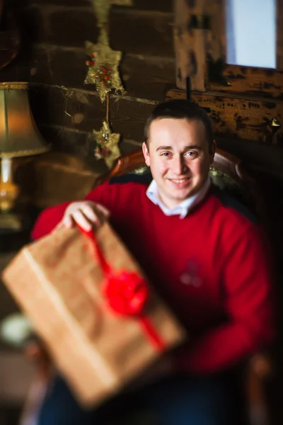 Junger Mann mit Geschenk neben Weihnachtsbaum und Geschenken — Stockfoto