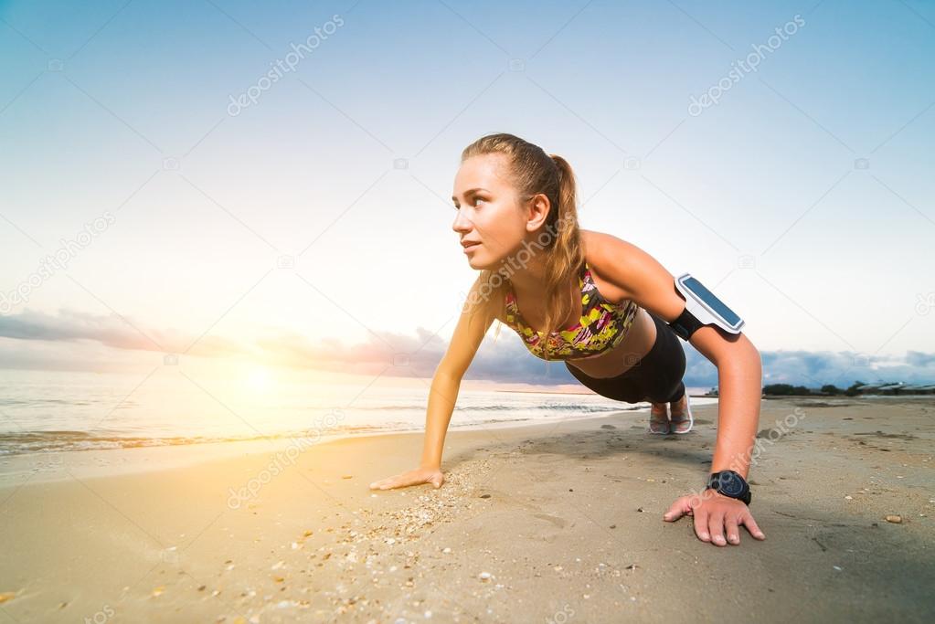 Sporty girl doing push ups on beach at sunrise