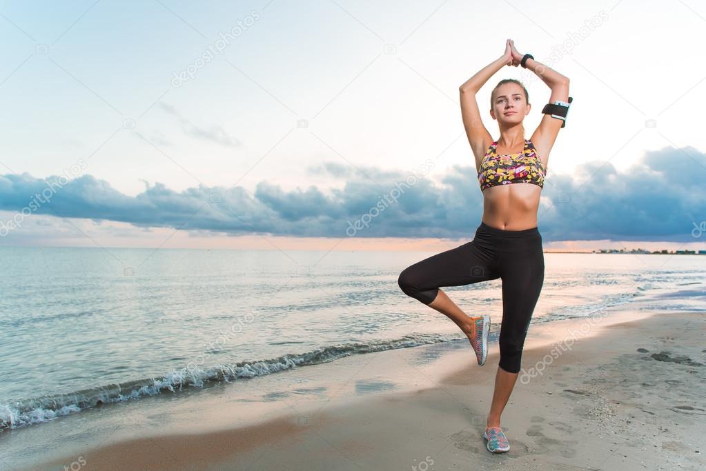 Young fit girl practicing yoga on beach at sunrise
