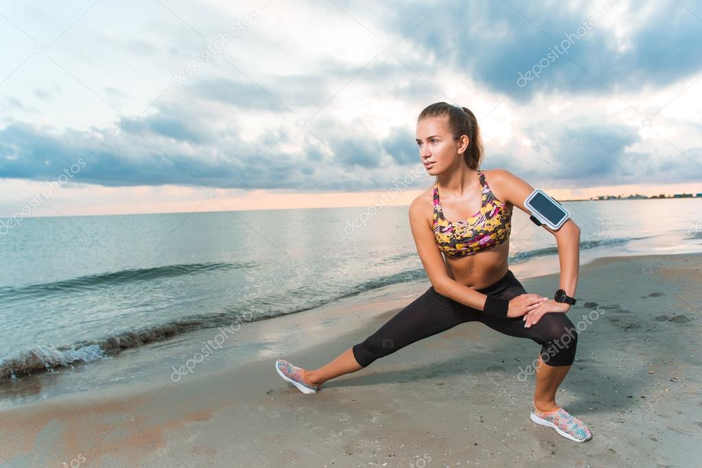Young fit girl stretching on beach at sunrise
