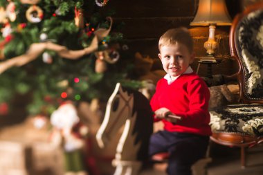 Küçük çocuk Noel ağacı önünde ahşap sallanan at binmek