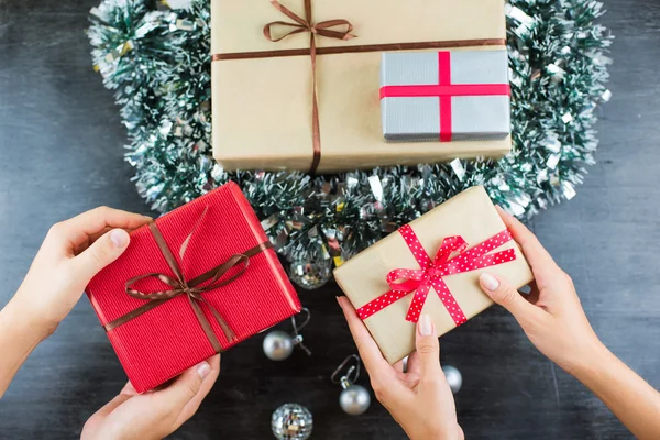 Regalos de Navidad en una mesa con fondo negro y manos sosteniendo regalos — Foto de Stock