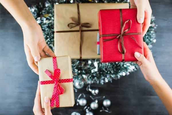 Regalos de Navidad en una mesa con fondo negro y manos sosteniendo regalos — Foto de Stock