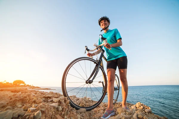 Ciclista feminina de pé em uma rocha e olhando para o mar — Fotografia de Stock
