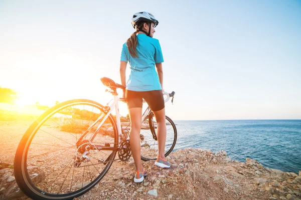 Ciclista feminina de pé em uma rocha e olhando para o mar — Fotografia de Stock