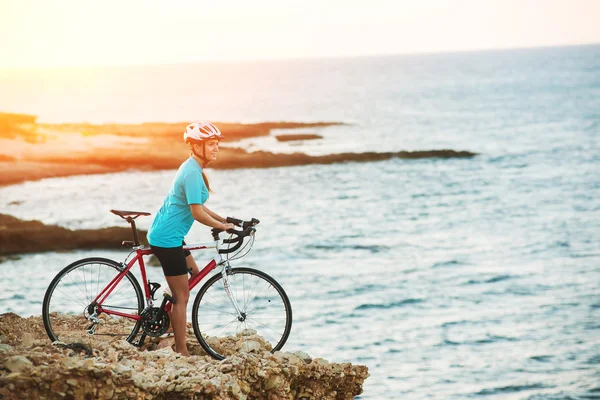 Vrouwelijke fietser staande op een rots en kijken naar zee — Stockfoto