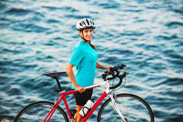 Ciclista feminina de pé em uma rocha e olhando para o mar — Fotografia de Stock