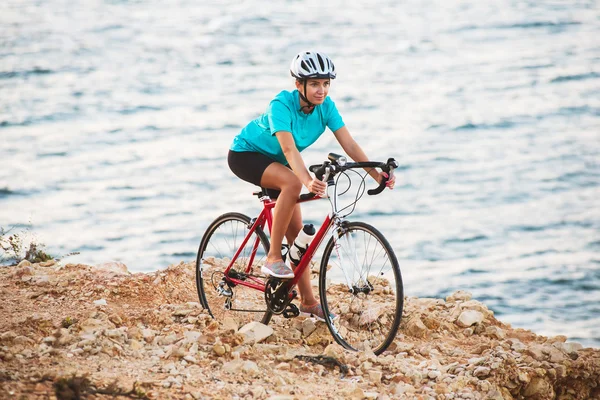 Vrouwelijke fietser staande op een rots met fiets en kijken naar zee — Stockfoto