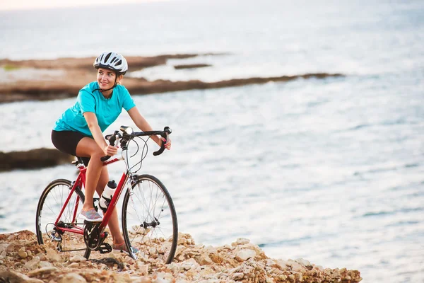 Vrouwelijke fietser staande op een rots met fiets en kijken naar zee — Stockfoto