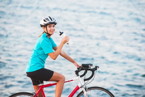 Vrouwelijke fietser drinkwater met zee op backgroound — Stockfoto