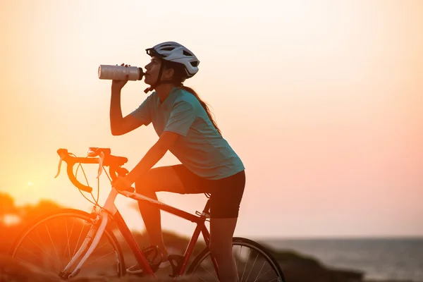 Silhouet van vrouwelijke fietser paardrijden fiets en dringking water met zee op de achtergrond — Stockfoto