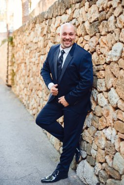 Koyu mavi ceketli yakışıklı damat. Taş bir duvarın arkasında poz vermek. Kaledeki damat..