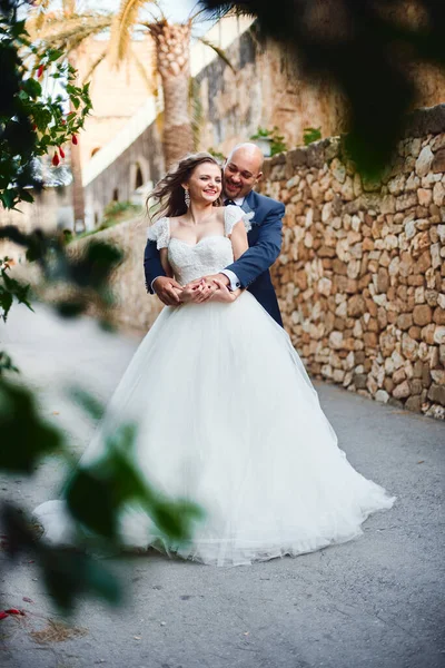 新婚旅行抱擁と笑顔 美しい緑の茂みや花を背景に城への入り口で — ストック写真