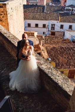 Gelin ve damat, eski şehrin arka planındaki kale duvarında sarılıyorlar.