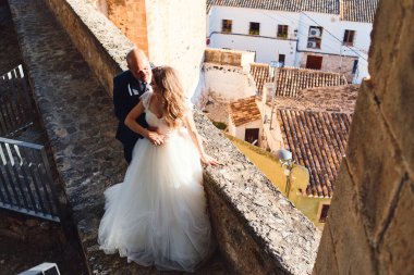 Gelin ve damat, eski şehrin arka planındaki kale duvarında sarılıyorlar.
