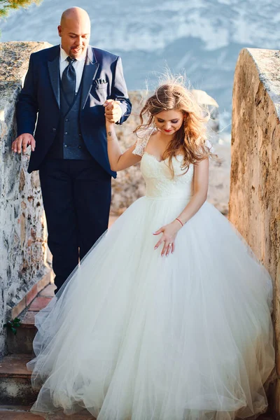 花嫁と新郎は山の背景に城の壁を歩いています — ストック写真