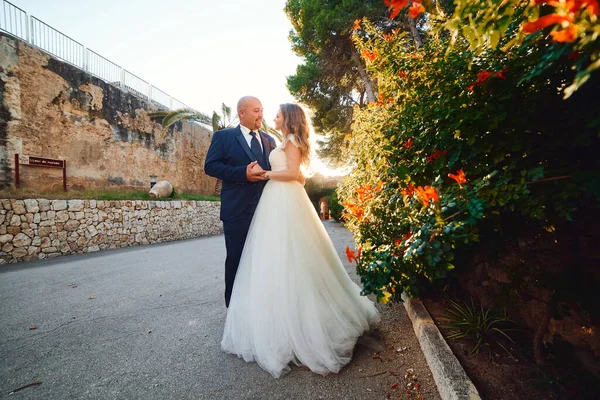 Newlyweds hug and smile, at the entrance to the castle against the background of a stone wall and palm trees