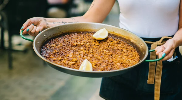 Bir garson elinde deniz ürünleriyle paella tutuyor.