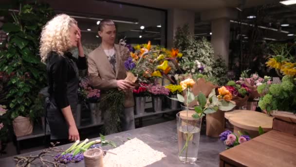 Молодой человек покупает букет в цветочном магазине — стоковое видео