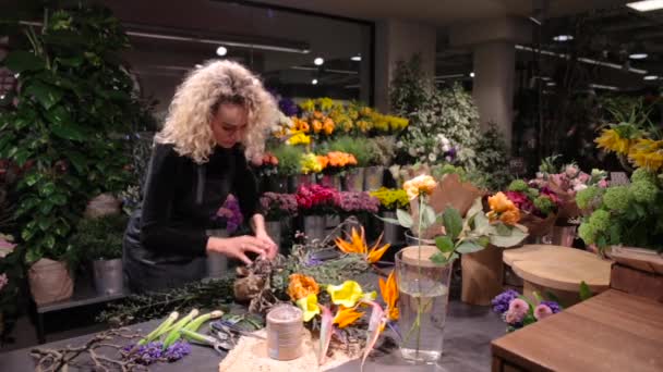 Beautiful woman florist making a bouquet at flower shop — Stock Video
