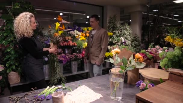 Молодой человек покупает букет в цветочном магазине — стоковое видео