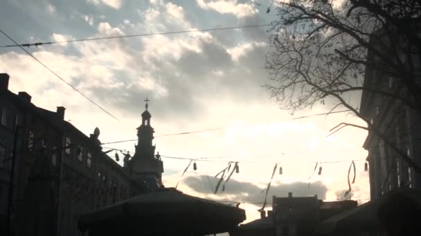 Wind develops ribbons on electric garland on a sky background and old town — Stock Video