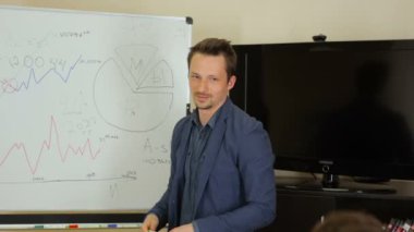 Toplantı odasında beyaz tahta yakınındaki toplantısında konuşuyor