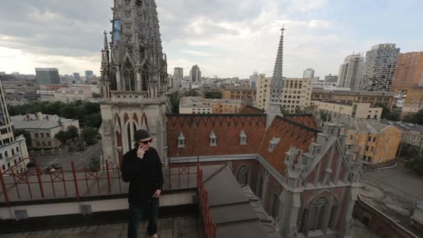 Hombre de negro hablando por teléfono en el techo del edificio cerca de la catedral católica fa — Vídeos de Stock
