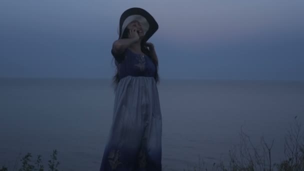 Девушка в шляпе на берегу с радостью разговаривает по телефону — стоковое видео