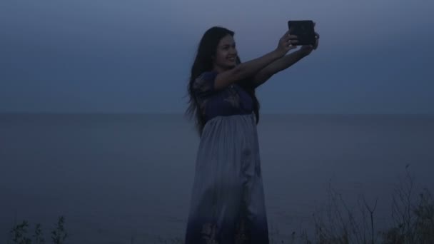 Девушка у моря фотографирует селфи на мини-планшете — стоковое видео