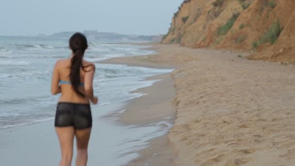 Chica trotando por la mañana a lo largo de la línea de surf de la playa de mar en verano — Vídeos de Stock