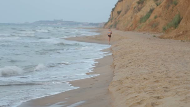 Chica trotando por la mañana a lo largo de la línea de surf de la playa de mar en verano — Vídeos de Stock