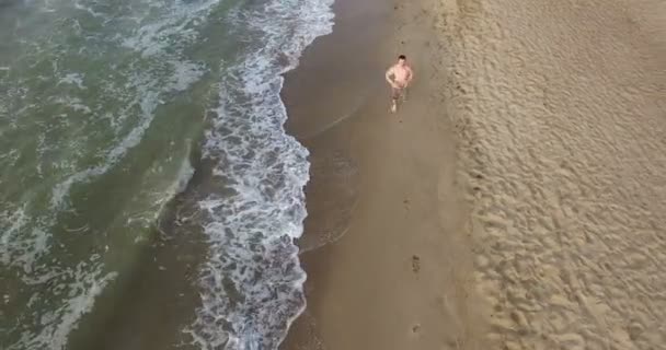 Chico trotando por la mañana a lo largo de la línea de surf de la playa de mar en verano — Vídeo de stock