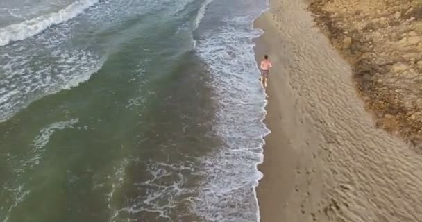 Chico trotando por la mañana a lo largo de la línea de surf de la playa de mar en verano — Vídeo de stock