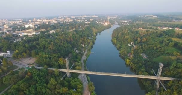 Puente colgante sobre el río entre la ciudad y el bosque — Vídeos de Stock