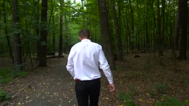 Junger Mann im weißen Hemd geht auf Waldweg — Stockvideo