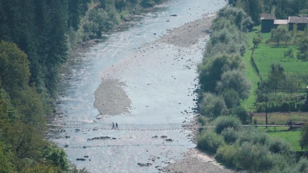 Familie fährt pedestische Hängebrücke über Gebirgsfluss in Dorf — Stockvideo