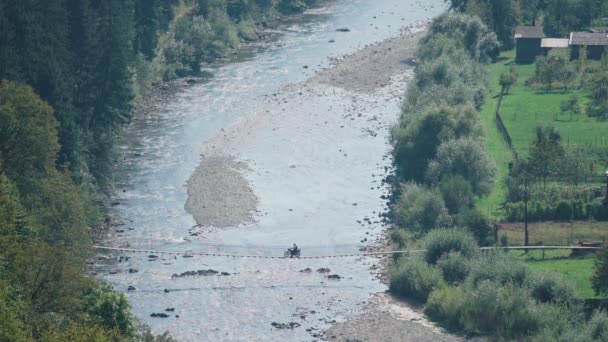 Radler bewegte Fußgängerhängebrücke über Gebirgsfluss im Dorf — Stockvideo