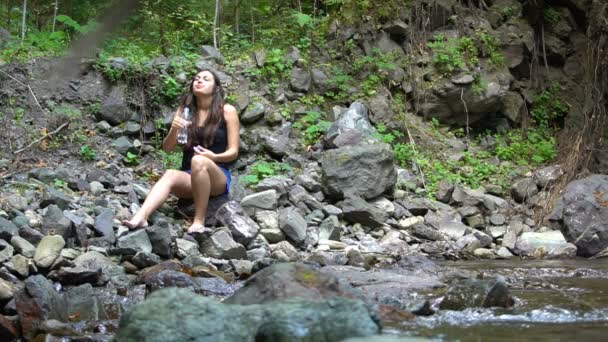 Fille boit de l'eau sur la rive de la rivière de montagne — Video